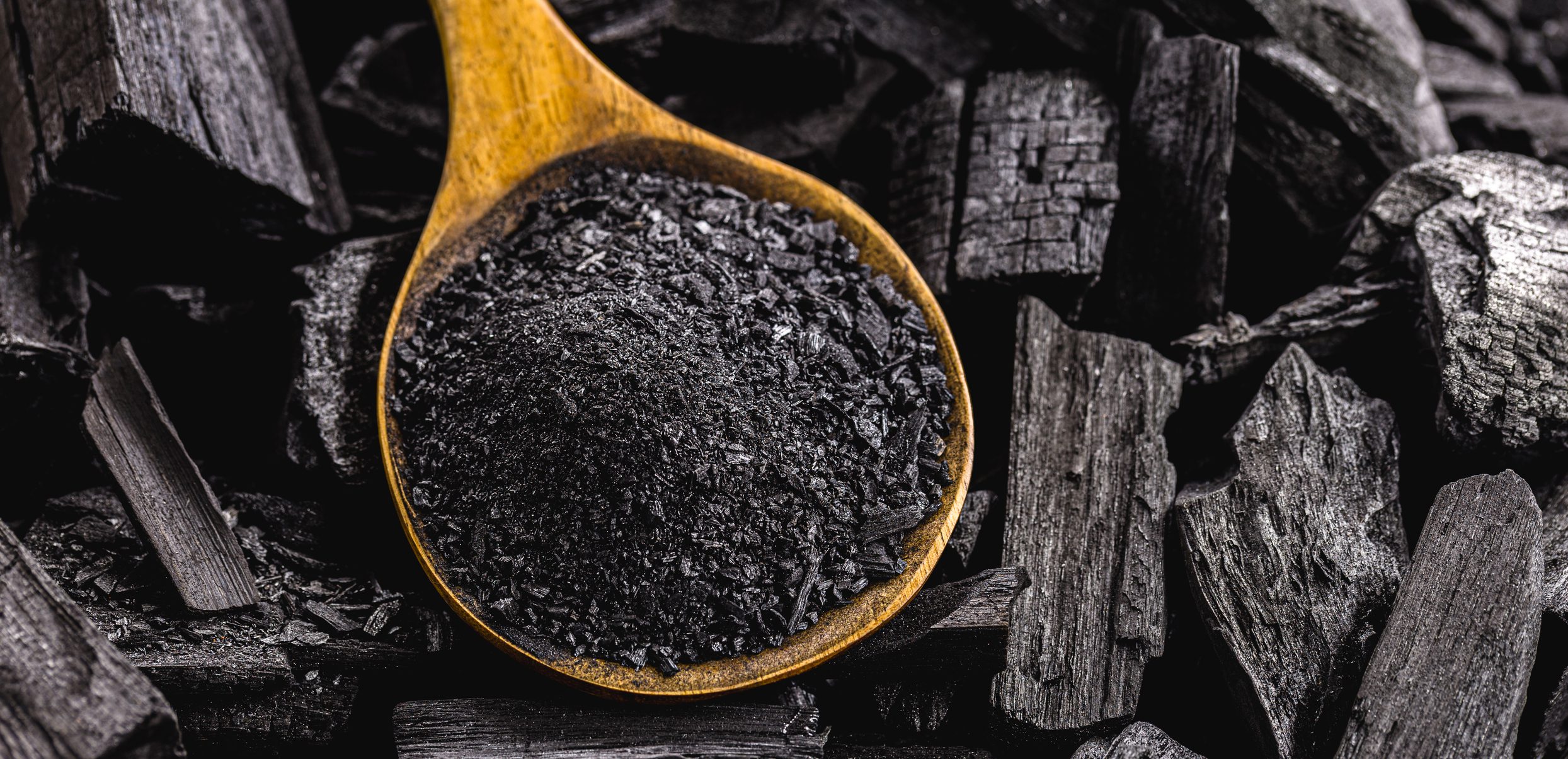 wooden spoon with coal dust on pieces of coal A wooden spoon filled with black charcoal.