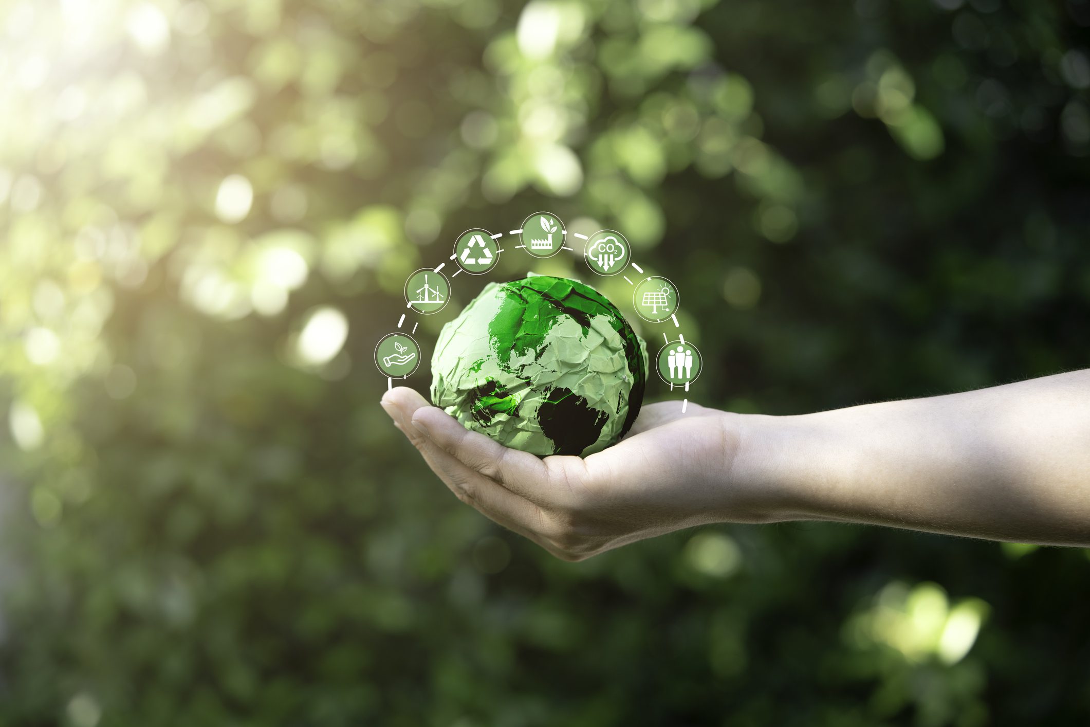 Businessman holding green scrap paper ball with world map and environment icon such as carbon reduction green factory recycle and solar cell for zero carbon emission credit to prevent global warming. A person holding a green globe in their hand.